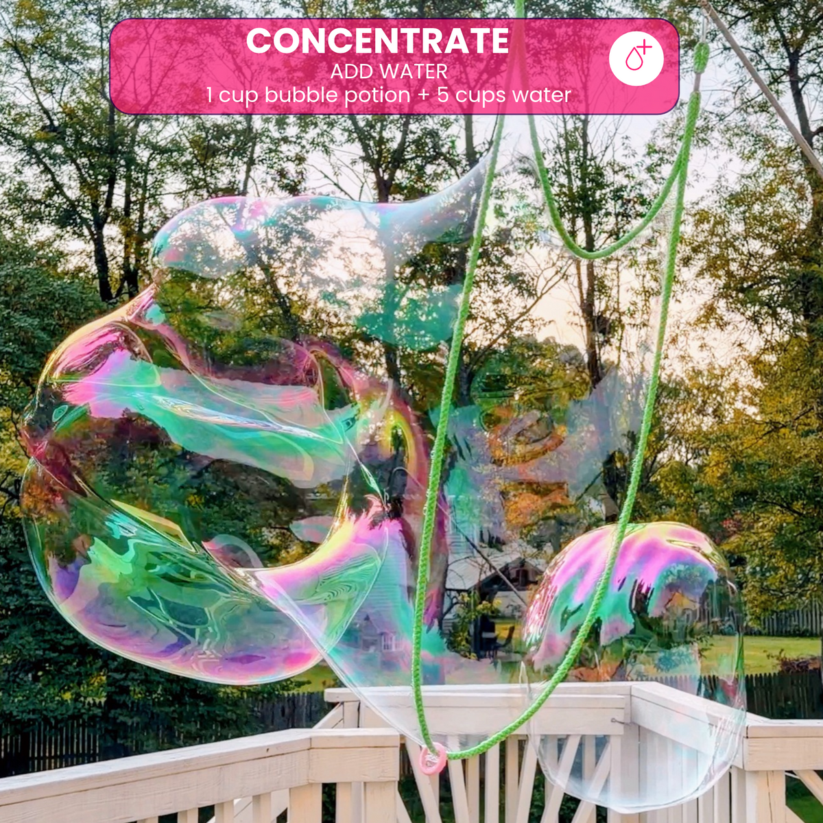 A large, colorful iridescent giant bubble being formed with green rope wands on an outdoor deck, labeled as One Two Celebrate ® Concentrate bubble mix