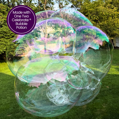 Close-up of a large, multi-layered cluster of iridescent bubbles reflecting soft pink, purple, and green light, created with the One Two Celebrate® Bubble Potion.