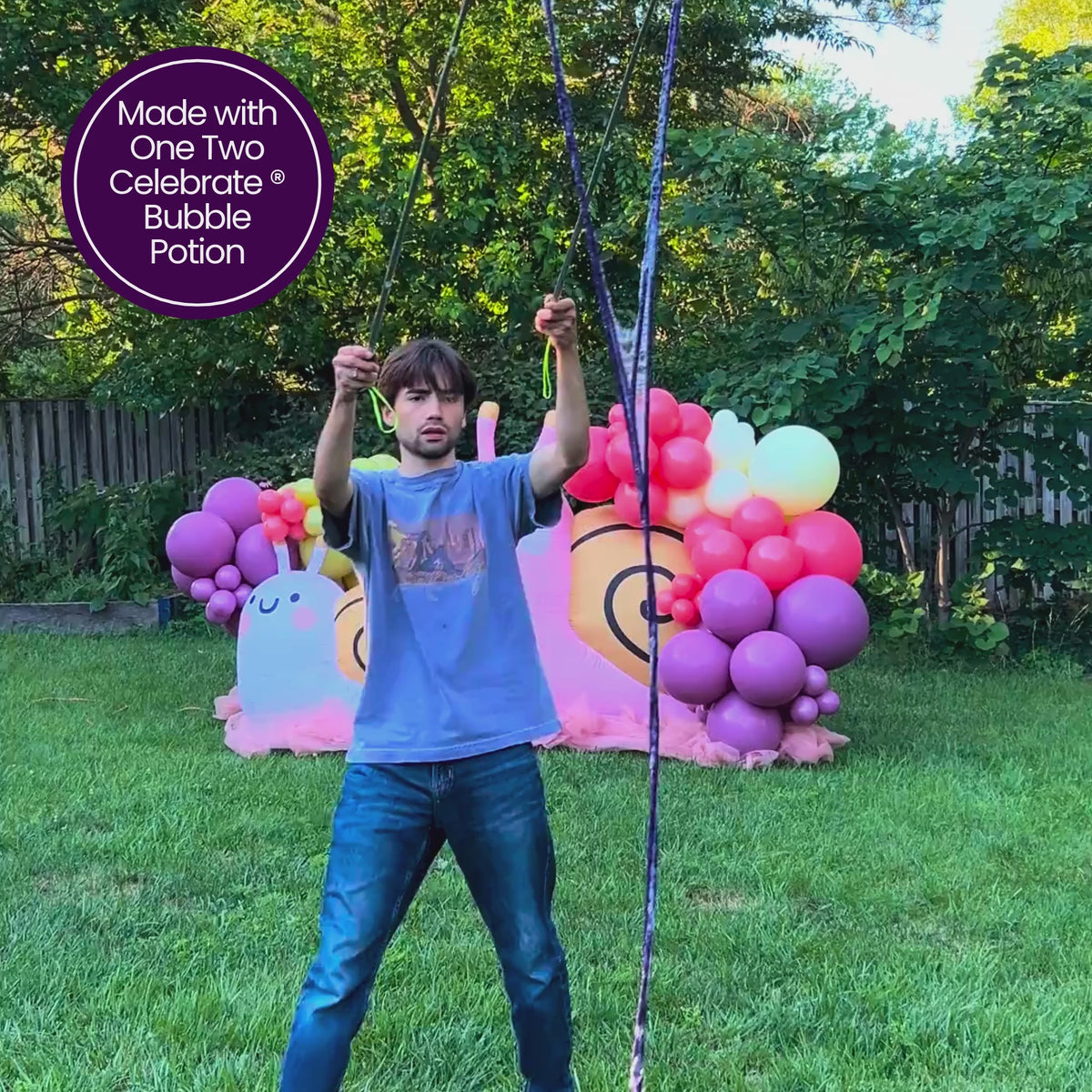 Giant bubble wands and One Two Celebrate® Bubble Potion in action creating massive iridescent bubbles at an outdoor party next to a custom Ploufe™ snail and balloon decor setup.